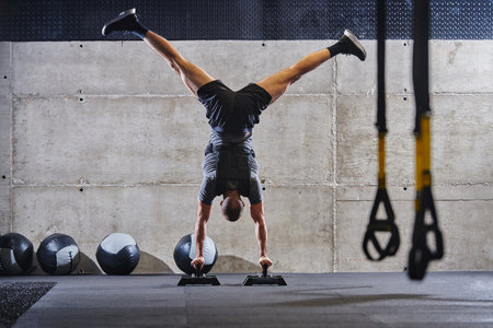 A muscular man in a handstand position, showcasing his exceptional balance and body control while performing a variety of exercises to enhance his overall body stability and strength in a modern gymの写真素材