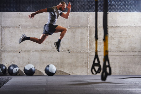 A muscular man captured in air as he jumps in a modern gym, showcasing his athleticism, power, and...