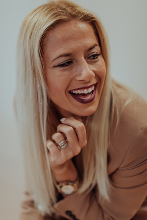 A confident and successful businesswoman, with a wide smile, strikes a pose in front of a beige background, exuding professionalism and eleganceの写真素材