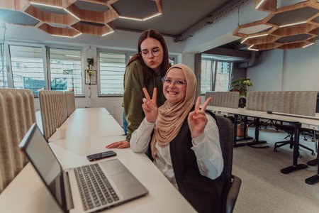 Young businesswomens, one of them wearing a hijab, are collaboratively problem-solving in a modern...
