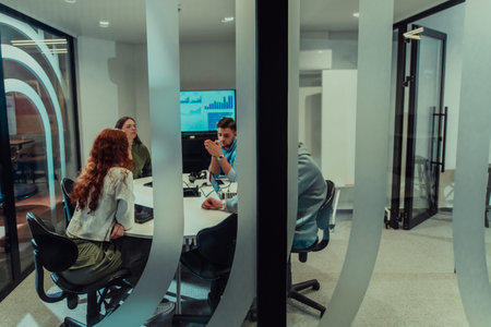 A group of young business entrepreneurs engages in a focused meeting, discussing various business strategies and collaboratively solving challenging problems, showcasing ambition, creativity, and teamwork in modern glass officeの写真素材