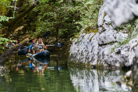 A young couple enjoying an idyllic kayak ride in the middle of a beautiful river surrounded by forest greeneryの写真素材