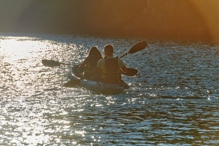 A young couple enjoying an idyllic kayak ride in the middle of a beautiful river surrounded by forest greenery in sunset timeの写真素材