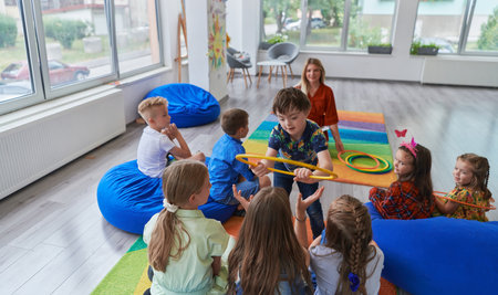 A happy female teacher sitting and playing hand games with a group of little schoolchildrenの写真素材