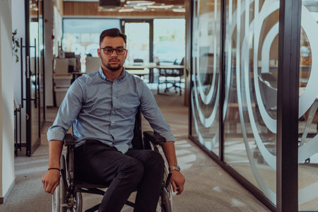 In a large modern corporation, a determined businessman in a wheelchair navigates through a hallway, embodying empowerment and inclusivity in the corporate world.の写真素材