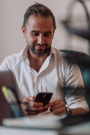 A businessman using on his smartphone while seated in an office, showcasing his professional demeanor and active communication.の写真素材