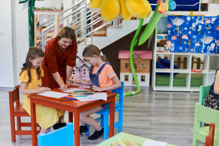Creative kids during an art class in a daycare center or elementary school classroom drawing with female teacher.の写真素材