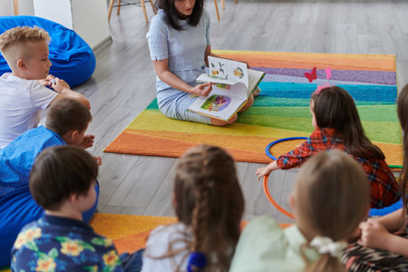 Reading time in an elementary school or kindergarten, a teacher reading a book to children in an elementary school or kindergarten. The concept of pre-school education. Selective focusの写真素材