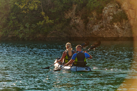 A young couple enjoying an idyllic kayak ride in the middle of a beautiful river surrounded by forest greenery in sunset timeの写真素材