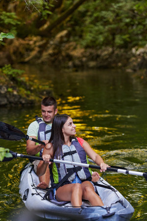 A young couple enjoying an idyllic kayak ride in the middle of a beautiful river surrounded by forest greeneryの写真素材