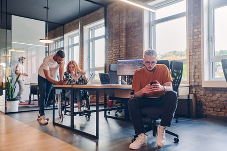 A diverse group of business professionals collaborates in a modern startup coworking center, utilizing a mix of paper-based and technological tools such as mobile phones and computers to collectively tackle a range of business challenges.の写真素材