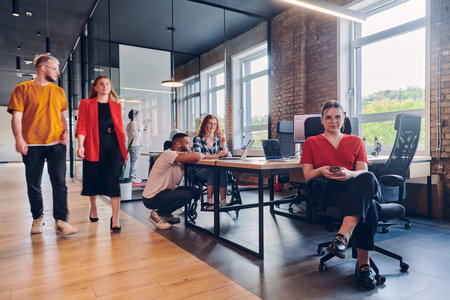 A diverse group of business professionals collaborates in a modern startup coworking center, utilizing a mix of paper-based and technological tools such as mobile phones and computers to collectively tackle a range of business challenges.の写真素材