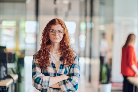 A portrait of a young businesswoman with modern orange hair captures her poised presence in a hallway of a contemporary startup coworking center, embodying individuality and professional confidence.の写真素材