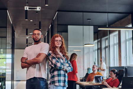 A young African American businessman and a modern businesswoman with orange hair stand side by side,...