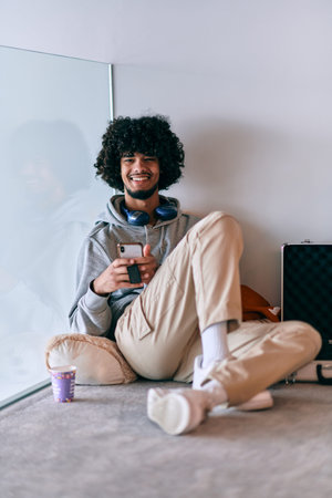 African-American entrepreneur taking a relaxing break from work, sitting on the floor while using wireless headphones and a smartphone for some digital entertainment.の写真素材