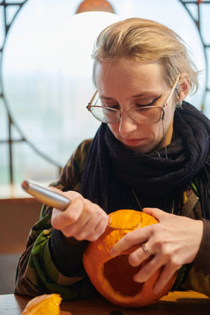 A modern blonde woman in military uniform is carving spooky pumpkins with a knife for Halloween nightの写真素材