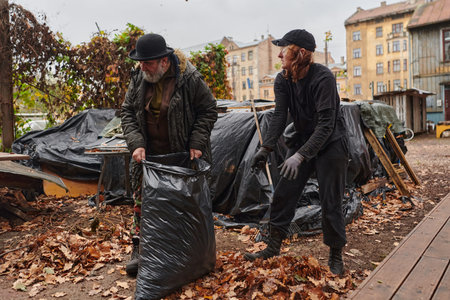 Father-daughter duo bonding in the garden as they work together to collect fallen leaves and fill up...