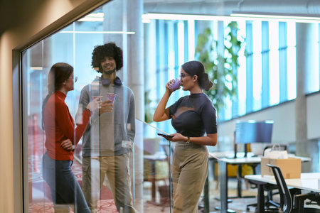 Amidst the modern glass walls of a startup office, a diverse group of colleagues, including an...