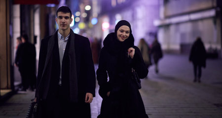 Happy multicultural business couple walking together outdoors in an urban city street at night near a jewelry shopping store window.の写真素材