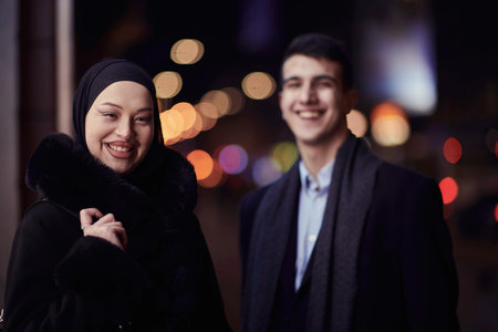 Happy multicultural business couple walking together outdoors in an urban city street at night near a jewelry shopping store window.の写真素材