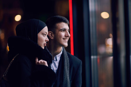 Happy multicultural business couple walking together outdoors in an urban city street at night near a jewelry shopping store window.の写真素材