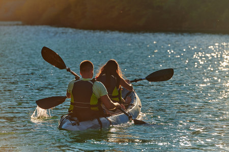 A young couple enjoying an idyllic kayak ride in the middle of a beautiful river surrounded by forest greenery in sunset timeの写真素材
