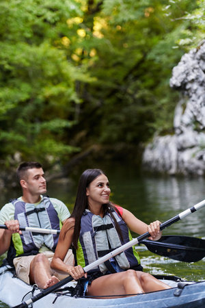 A young couple enjoying an idyllic kayak ride in the middle of a beautiful river surrounded by forest greeneryの写真素材