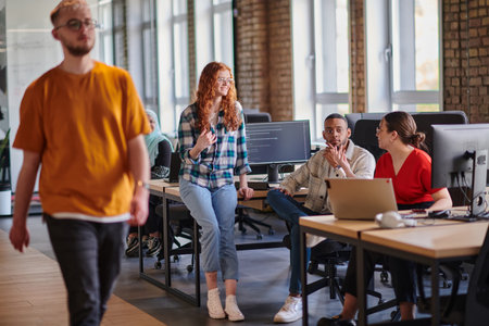 A diverse group of young business individuals congregates in a modern startup coworking center,...