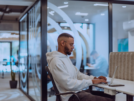 In a modern office setting, an African American businessman is diligently working on his laptop, embodying determination, ambition, and productivity in his professional environmenの写真素材
