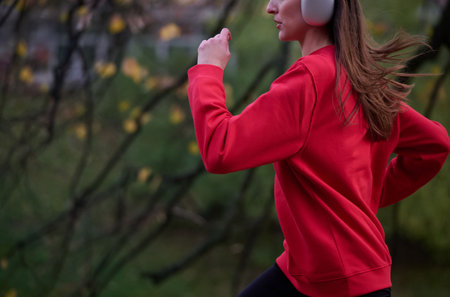 Young beautiful woman running in autumn park and listening to music with headphones on smartphoneの写真素材