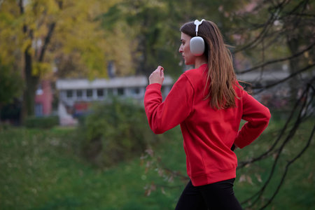 Young beautiful woman running in autumn park and listening to music with headphones on smartphoneの写真素材