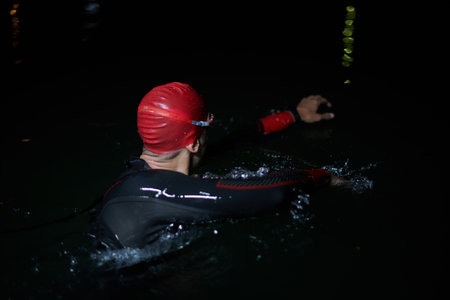 A determined professional triathlete undergoes rigorous night time training in cold waters, showcasing dedication and resilience in preparation for an upcoming triathlon swim competitionの写真素材