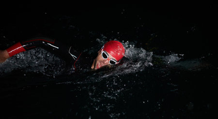 A determined professional triathlete undergoes rigorous night time training in cold waters, showcasing dedication and resilience in preparation for an upcoming triathlon swim competitionの写真素材