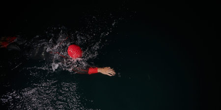 A determined professional triathlete undergoes rigorous night time training in cold waters,...