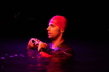 Authentic triathlete swimmer having a break during hard training on night neon gel light