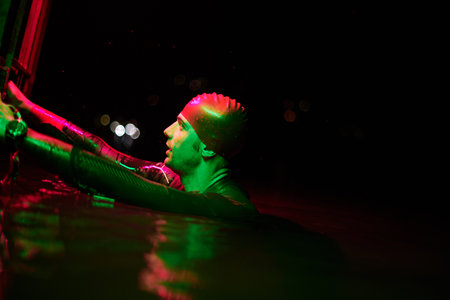 authentic triathlete swimmer having a break during hard training on night neon gel lightの写真素材