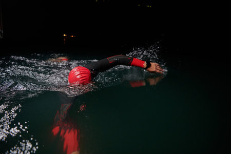 A determined professional triathlete undergoes rigorous night time training in cold waters, showcasing dedication and resilience in preparation for an upcoming triathlon swim competitionの写真素材