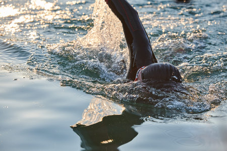 Triathlon athlete swimming on lake in sunrise wearing wetsuitの写真素材