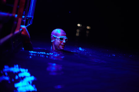 authentic triathlete swimmer having a break during hard training on night neon gel lightの写真素材