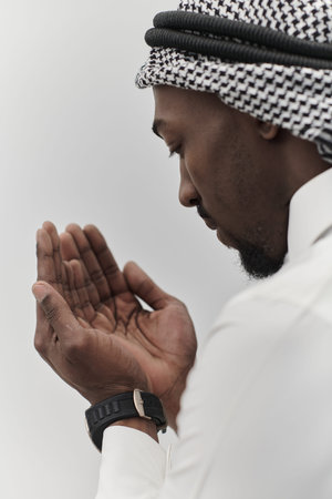 African American Muslim man raises his hands in prayer, seeking solace and devotion to God, as he stands isolated against a serene white backdrop, symbolizing a profound expression of faith and contemplationの写真素材