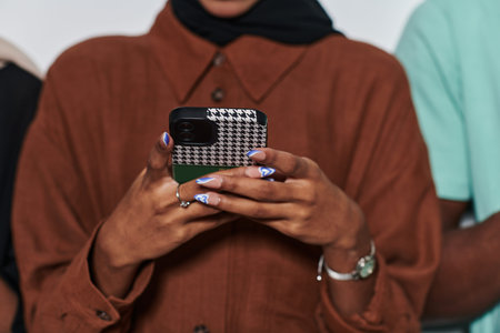 Captured in a close-up moment, a girl in hijab skillfully engages with her smartphone, reflecting a...