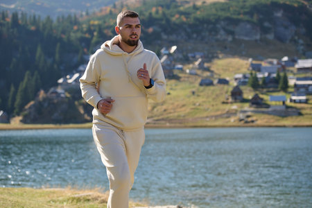 Athletic man maintains his healthy lifestyle by running through the scenic mountain and lakeside environment, showcasing a commitment to fitness and well-beingの写真素材