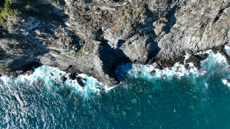 Aerial footage of turquoise ocean waters washing rugged, rocky shorelineの写真素材