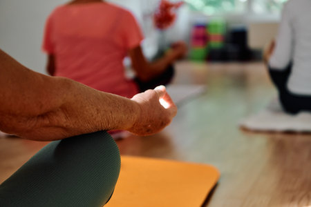 In this sunlit space, a senior womans hand gracefully engages in various yoga poses, embodying the essence of active aging, health, and inner peaceの写真素材
