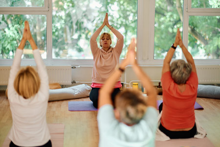 A group of senior women engage in various yoga exercises, including neck, back, and leg stretches,...