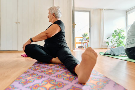An elderly woman gracefully engages in various yoga poses, stretching her limbs and finding serenity in a modern sunlit space under the guidance of a trained instructor, embodying the essence of active and mindful agingの写真素材