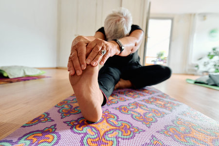 An elderly woman gracefully engages in various yoga poses, stretching her limbs and finding serenity in a modern sunlit space under the guidance of a trained instructor, embodying the essence of active and mindful agingの写真素材