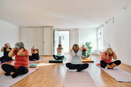 A group of senior women engage in various yoga exercises, including neck, back, and leg stretches,...