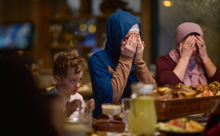 In a modern restaurant setting, a European Islamic family comes together for iftar during Ramadan, engaging in prayer before the meal, uniting tradition and contemporary practices in a celebration of faith and familyの写真素材