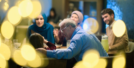 Grandparents arrive at their childrens and grandchildrens gathering for iftar in a restaurant during the holy month of Ramadan, bearing gifts and sharing cherished moments of love, unity, and cultural exchange, as they eagerly await their meal togetherの写真素材